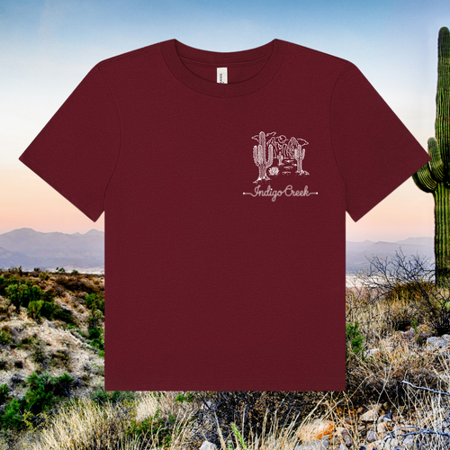 Maroon t-shirt with a logo and text on a desert landscape background