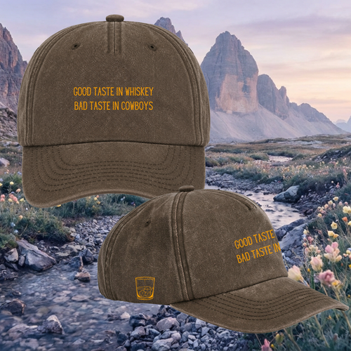 Two brown baseball caps with yellow embroidered text reading 'GOOD TASTE IN WHISKEY BAD TASTE IN COWBOYS' and a small whiskey glass logo, shown over a mountain landscape background.