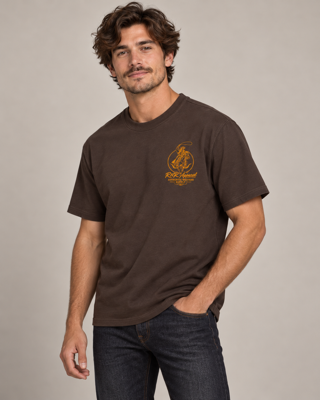 A man wearing a dark brown short-sleeve t-shirt with a orange  'Ride Local' graphic on the left chest, paired with dark blue jeans, against a solid light gray background.