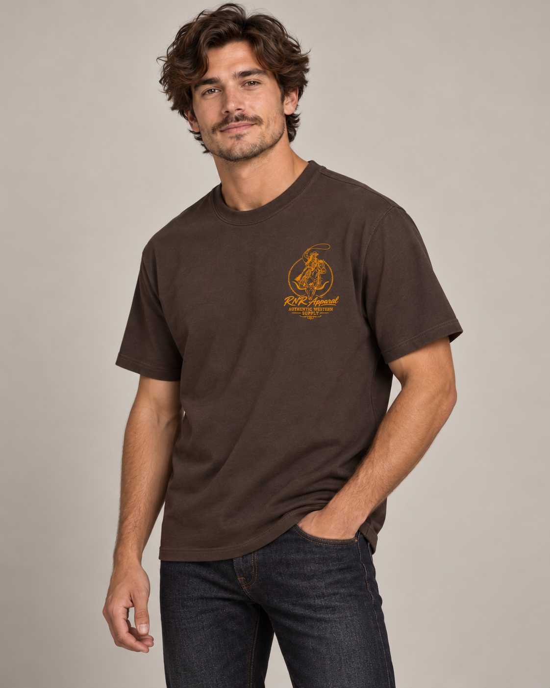 A man wearing a dark brown short-sleeve t-shirt with a orange  'Ride Local' graphic on the left chest, paired with dark blue jeans, against a solid light gray background.