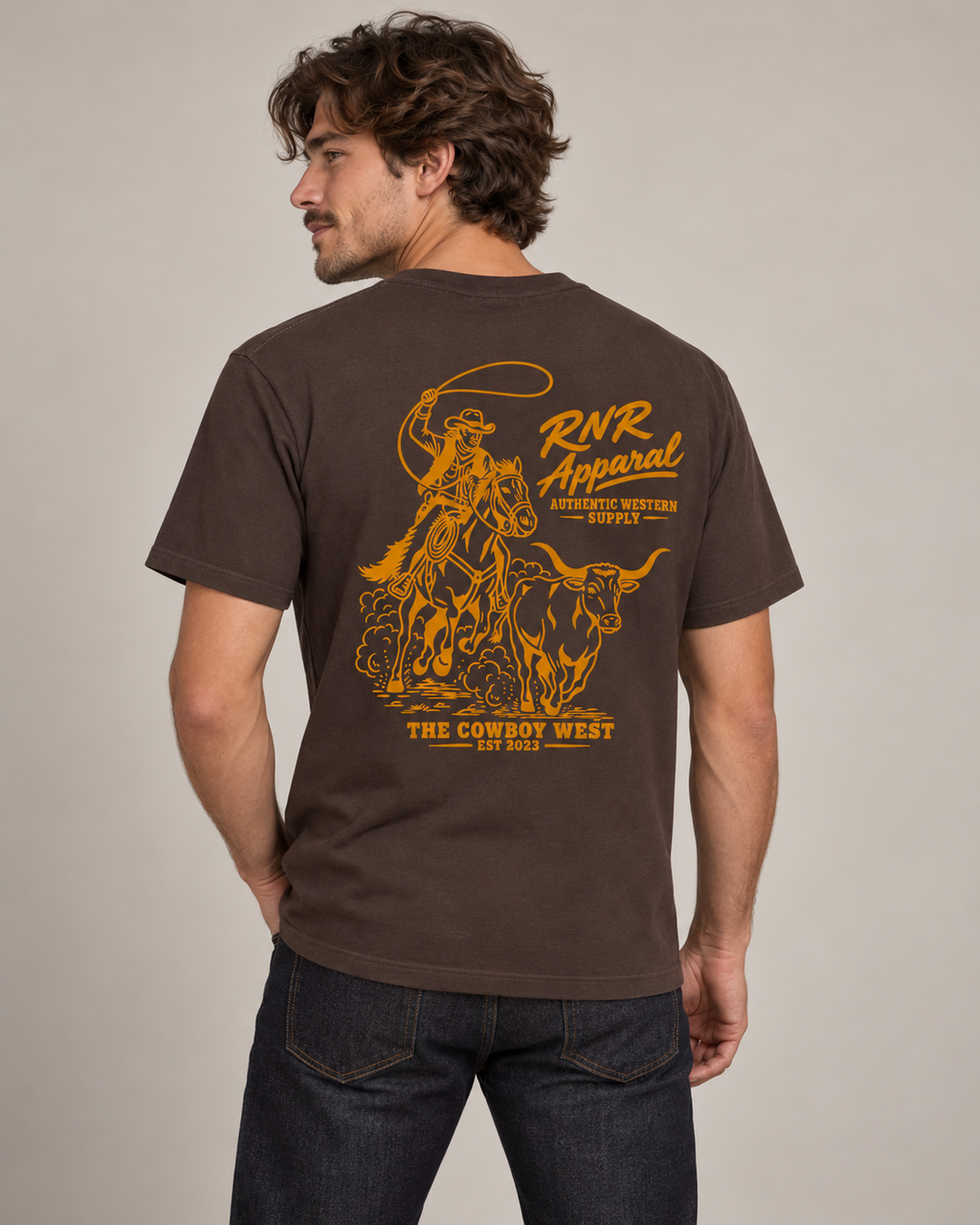 A man wearing a brown short-sleeve t-shirt with a large yellow graphic print on the back, featuring a cowboy and steer design with the text 'RNR Apparel' and 'The Cowboy West'.