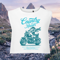 White sleeveless crop top with a teal graphic print of a woman riding a motorcycle and the text 'Country Roads' and 'Give a girl the right pair of boots and she can conquer the world', shown against a mountain landscape background.