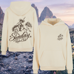 Cream-colored pullover hoodie shown from both front and back against a scenic mountain backdrop. The back features a large black graphic of a cowboy riding a horse with the text 'Sunday Rodeo Club', and the front has a smaller matching chest graphic.