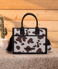 Handbag with cow print design and 'Wrangler' branding on a wooden surface.
